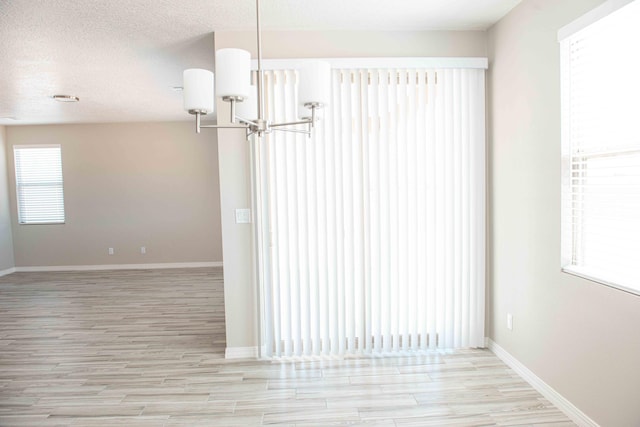 unfurnished dining area with an inviting chandelier, baseboards, light wood-style floors, and a textured ceiling