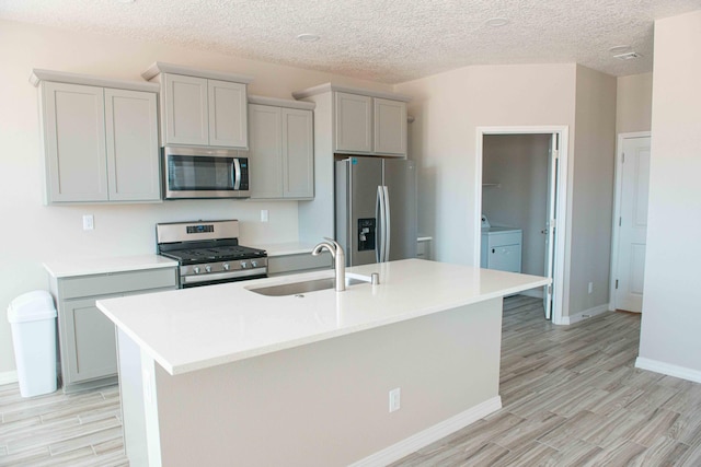 kitchen featuring a sink, light countertops, light wood finished floors, stainless steel appliances, and an island with sink