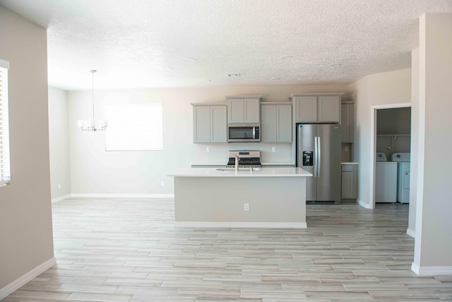 kitchen featuring appliances with stainless steel finishes, light wood finished floors, a textured ceiling, and washer and clothes dryer
