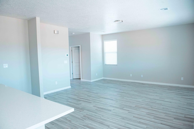 unfurnished room with a textured ceiling, baseboards, and light wood-style floors