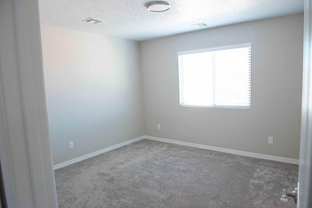 unfurnished room with carpet floors, a textured ceiling, visible vents, and baseboards