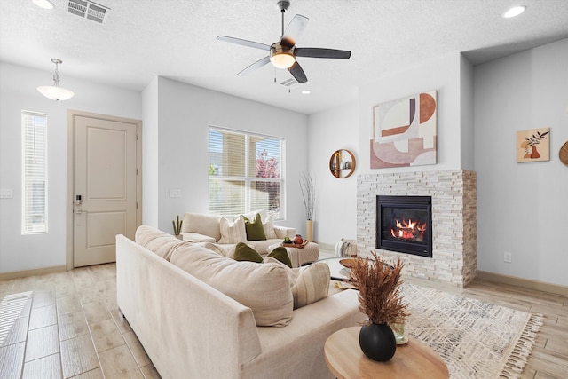 living area featuring light wood-style floors, ceiling fan, a textured ceiling, and visible vents