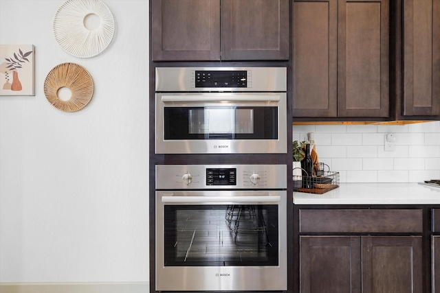 kitchen featuring light countertops, tasteful backsplash, double oven, and dark brown cabinets