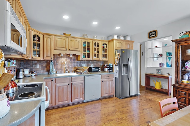 kitchen featuring a sink, light wood finished floors, white appliances, decorative backsplash, and glass insert cabinets