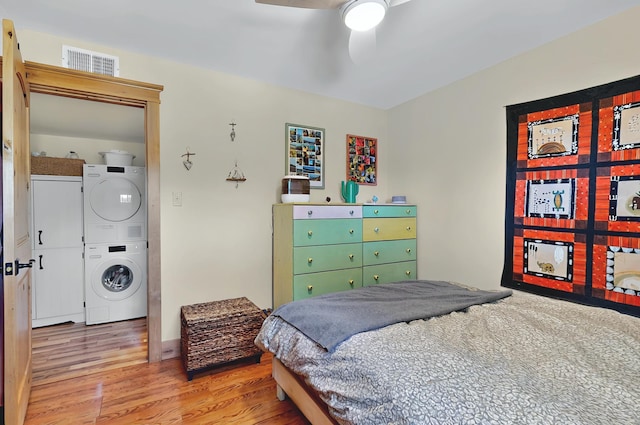 bedroom with stacked washing maching and dryer, a ceiling fan, wood finished floors, and visible vents