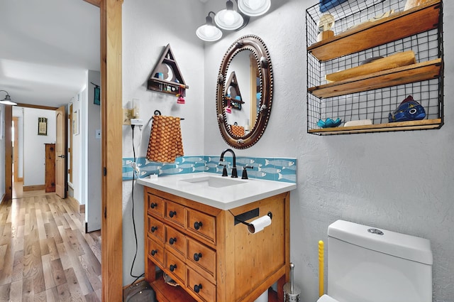 half bath with vanity, a textured wall, toilet, and wood finished floors