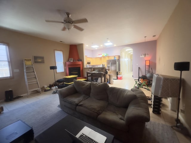 living area featuring arched walkways, plenty of natural light, a ceiling fan, and light tile patterned flooring