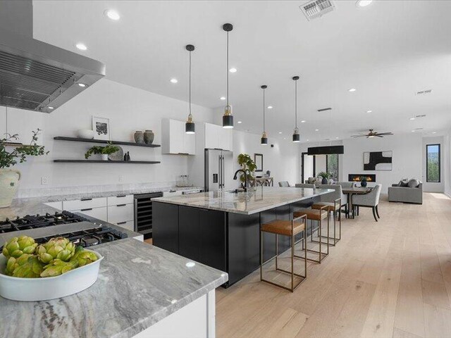 19 Anasazi Trl, Sandia Park, NM 87047 - kitchen featuring open shelves, stainless steel fridge, beverage cooler, wall chimney exhaust hood, and visible vents