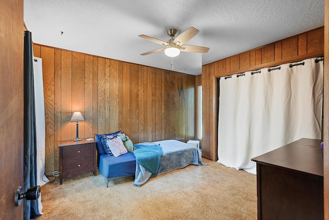 bedroom with wooden walls, a ceiling fan, a textured ceiling, and light carpet