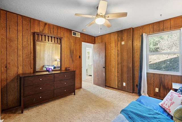 carpeted bedroom featuring visible vents, wood walls, and a ceiling fan