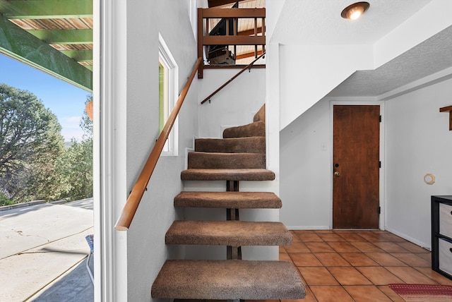 stairway with tile patterned floors, baseboards, and a textured ceiling
