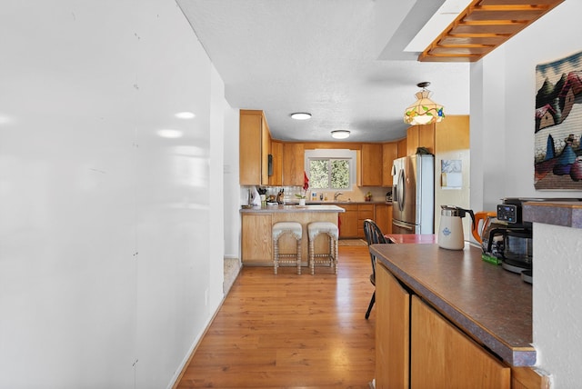kitchen featuring dark countertops, stainless steel fridge with ice dispenser, a kitchen breakfast bar, light wood-style flooring, and a peninsula