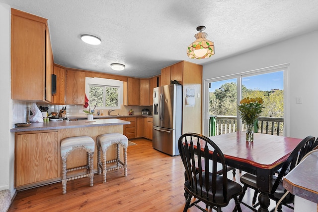 kitchen featuring a textured ceiling, a sink, stainless steel fridge with ice dispenser, a peninsula, and light wood-style floors
