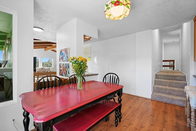 dining room with wood finished floors, attic access, stairway, a textured ceiling, and lofted ceiling with beams