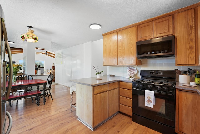kitchen with ceiling fan, black gas stove, stainless steel microwave, a peninsula, and light wood-style flooring