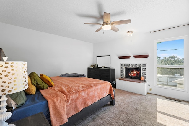 bedroom with ceiling fan, a lit fireplace, a textured ceiling, visible vents, and carpet