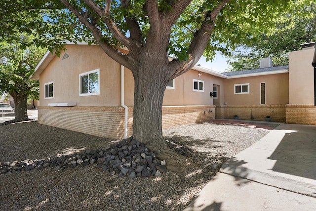 view of side of home with brick siding, stucco siding, a patio, and fence