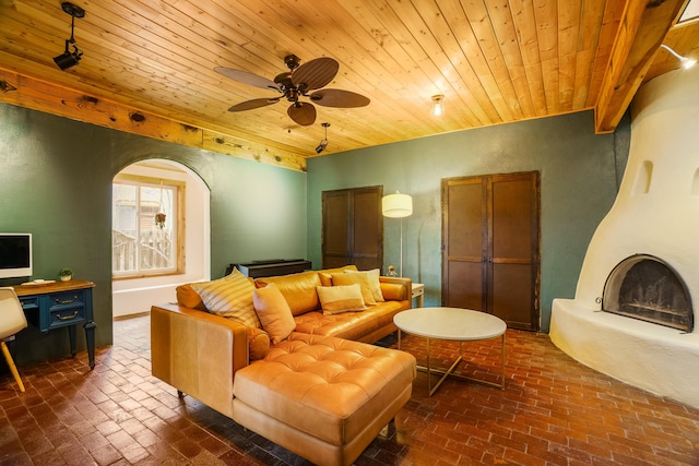 living area with a ceiling fan, wood ceiling, and brick floor