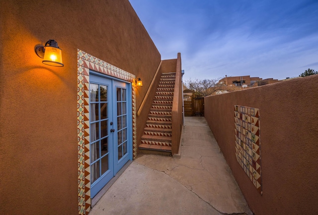 view of side of home with fence, french doors, stairs, and stucco siding