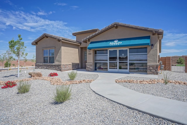 view of front facade featuring stucco siding, stone siding, and fence