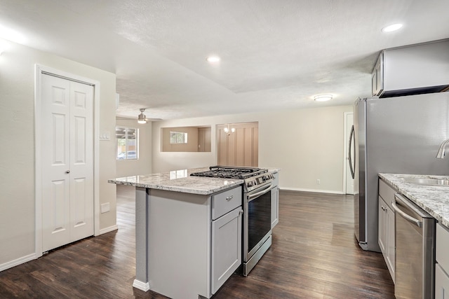 kitchen featuring dark wood-style flooring, light stone counters, a center island, stainless steel appliances, and baseboards