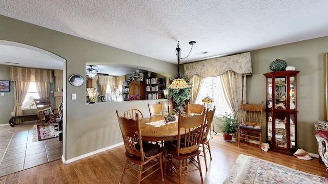 dining space with a textured ceiling, a wealth of natural light, arched walkways, and baseboards