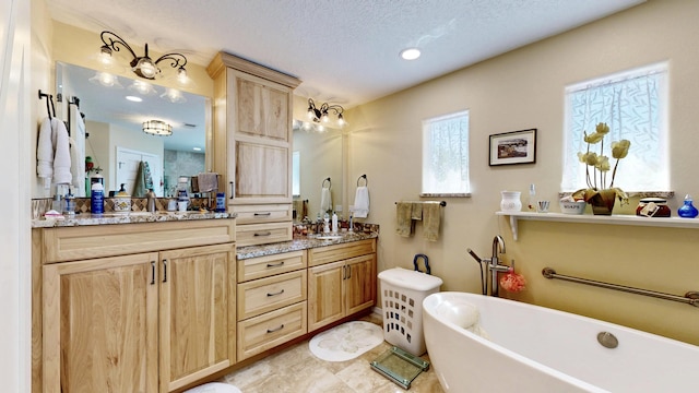 full bathroom with a textured ceiling, a freestanding tub, a sink, and double vanity