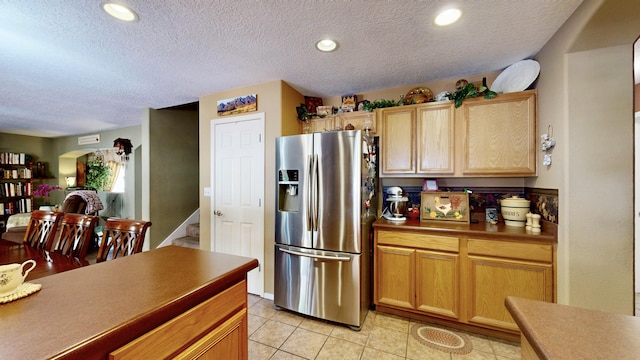 kitchen with light tile patterned floors, dark countertops, open floor plan, stainless steel refrigerator with ice dispenser, and a textured ceiling