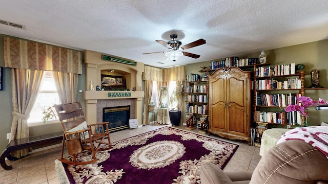 living area featuring light tile patterned flooring, a ceiling fan, visible vents, and a tile fireplace