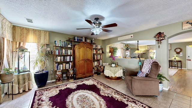 living area with a textured ceiling, visible vents, ceiling fan, light tile patterned flooring, and arched walkways