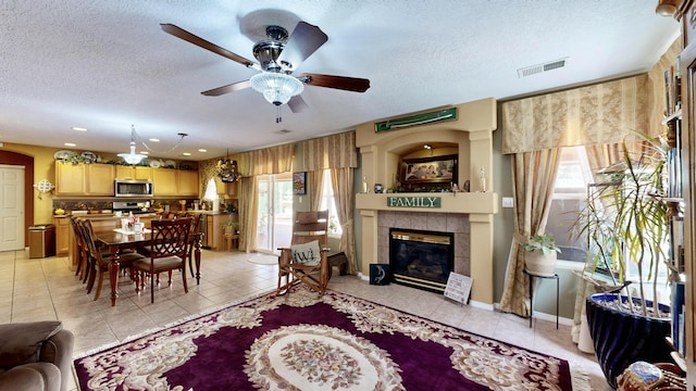 living area featuring light tile patterned floors, ceiling fan, visible vents, and a textured ceiling
