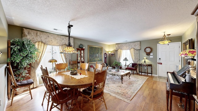 dining area featuring a textured ceiling, baseboards, light wood-type flooring, and visible vents