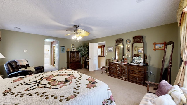 carpeted bedroom featuring arched walkways, a textured ceiling, visible vents, and a ceiling fan