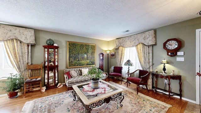 living room with a textured ceiling, visible vents, wood finished floors, and baseboards