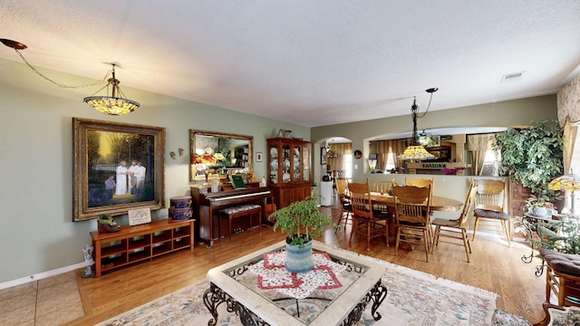 living area featuring wood finished floors, a textured ceiling, visible vents, arched walkways, and baseboards