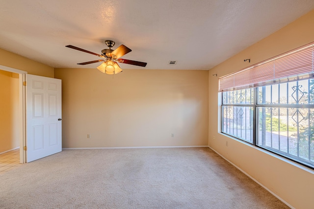 empty room with light colored carpet, a ceiling fan, baseboards, and visible vents