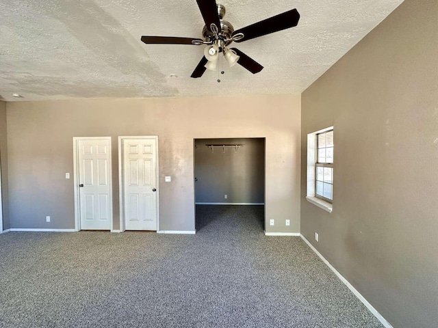 unfurnished bedroom with baseboards, a walk in closet, a textured ceiling, a ceiling fan, and carpet