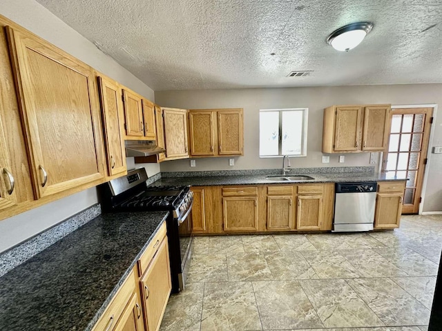 kitchen with a textured ceiling, visible vents, appliances with stainless steel finishes, a sink, and under cabinet range hood
