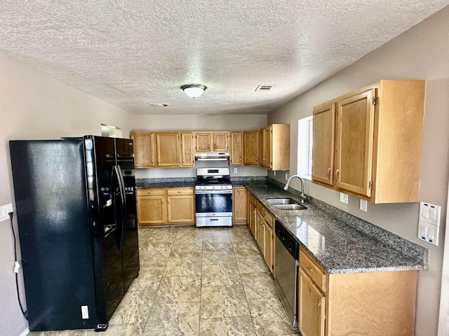 kitchen with a textured ceiling, a sink, dark stone countertops, under cabinet range hood, and stainless steel appliances