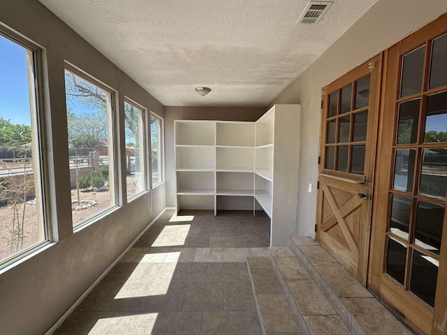 unfurnished sunroom with a textured ceiling, visible vents, and baseboards