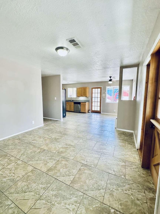 unfurnished living room with visible vents, a textured ceiling, baseboards, and stone finish flooring
