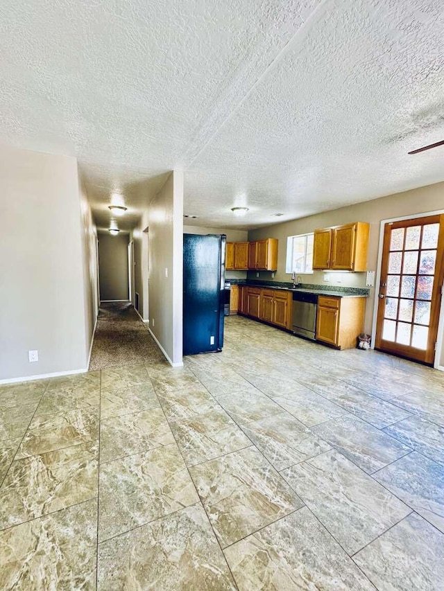 kitchen featuring stainless steel dishwasher, freestanding refrigerator, brown cabinetry, and baseboards