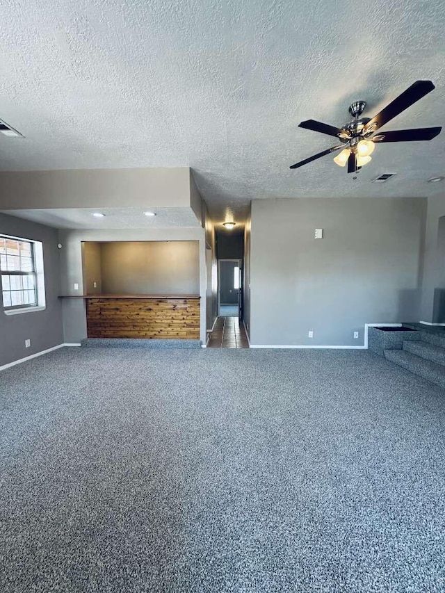 unfurnished living room with baseboards, carpet flooring, a textured ceiling, and visible vents