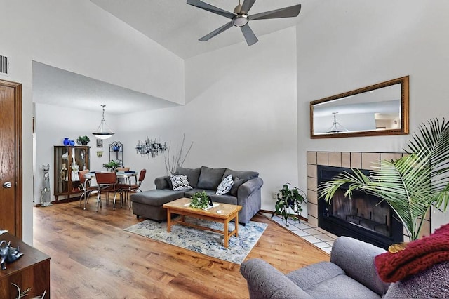 living area with ceiling fan, visible vents, a tile fireplace, wood finished floors, and high vaulted ceiling