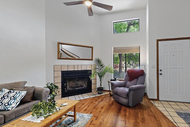 living room featuring a tiled fireplace, a towering ceiling, ceiling fan, and a healthy amount of sunlight