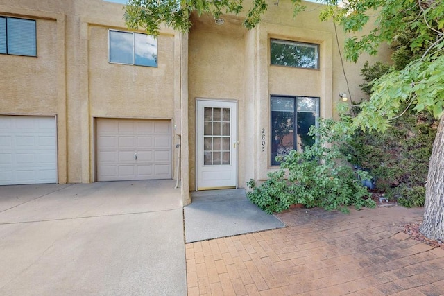 doorway to property featuring concrete driveway, an attached garage, and stucco siding