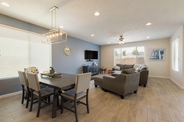 dining area featuring ceiling fan with notable chandelier, baseboards, a textured ceiling, and light wood-style flooring