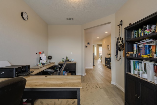 office space with a textured ceiling, baseboards, visible vents, and light wood-style flooring
