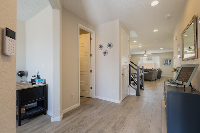 corridor with light wood-type flooring, recessed lighting, baseboards, and a textured ceiling
