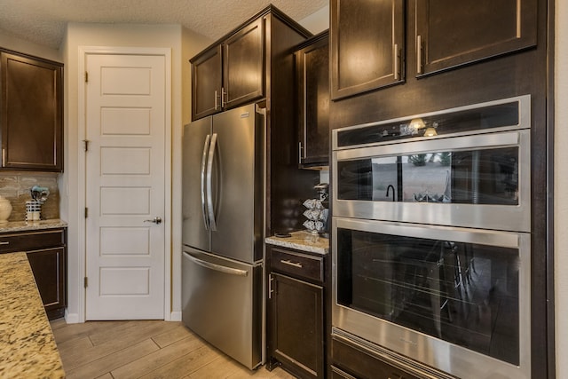 kitchen featuring backsplash, dark brown cabinets, light stone counters, light wood-style floors, and stainless steel appliances